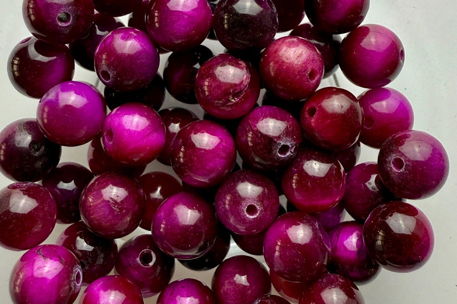 Runde, glänzende Tigerauge-Perlen in kräftigem Pink bis Magenta, stilvoll arrangiert in einer Schale.
