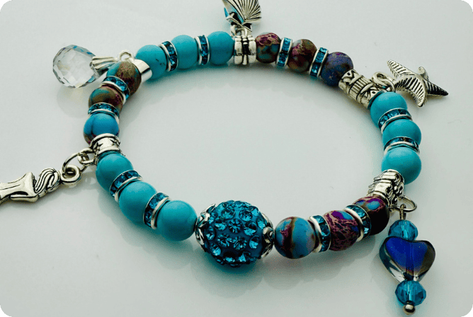 Armband im Meeresdesign mit Türkistönen, Jaspis-Perlen und Anhängern in Form von Meerjungfrau, Muschel und Fisch. Handgefertigt mit maritimen Details und funkelnden Kristallen – ideal für sommerliche Outfits.