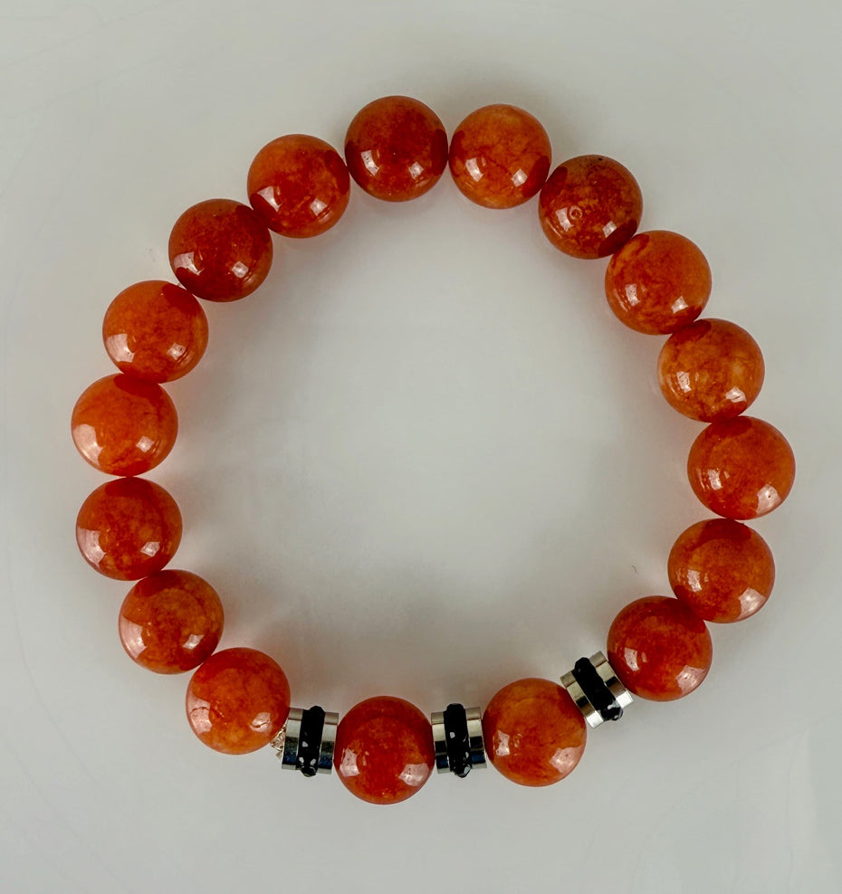 Handgefertigtes Armband mit leuchtenden Karneol-Quarz-Perlen in Orange-Rot, verziert mit eleganten Edelstahl-Elementen und funkelnden schwarzen Kristallakzenten. Ein modernes Accessoire mit lebendigen Farben und hochwertiger Verarbeitung.