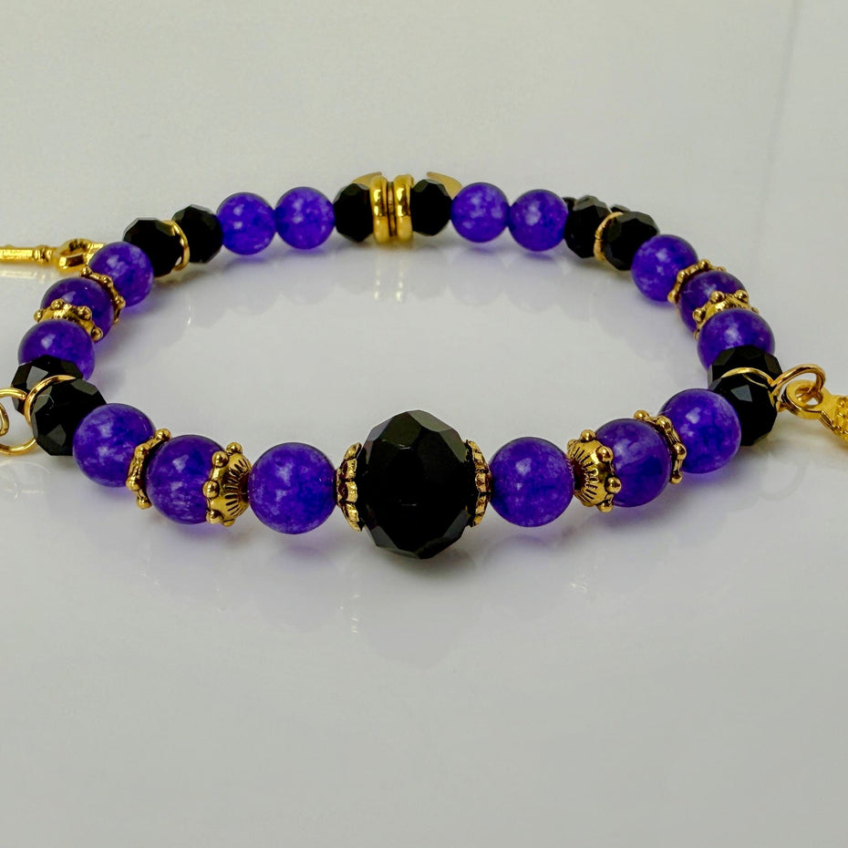 Elegantes Armband ‚Lila Traum‘ mit leuchtend lila Steinperlen, facettierten schwarzen Glasperlen und goldenen Akzenten. Verziert mit Anhängern wie einem goldenen Mond und einem Engelsflügel – ein luxuriöses, handgefertigtes Schmuckstück aus der Schweiz.