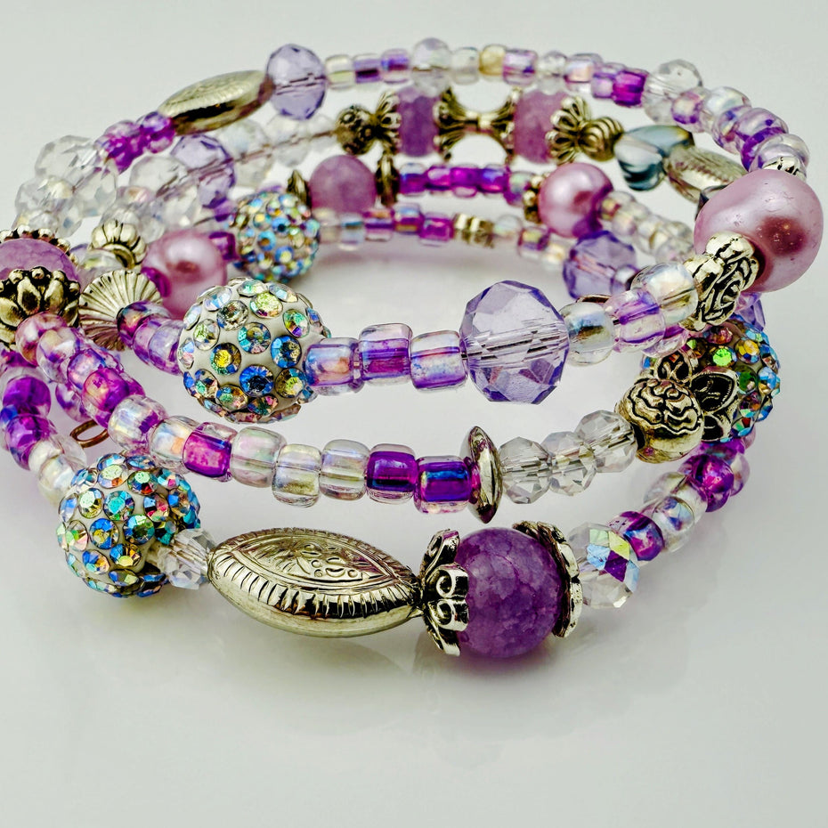Handgefertigtes Spiralarmband in zarten Rosa- und Fliedertönen mit funkelnden Glasperlen, Strass-Elementen und filigranen Metall-Details. Flexibel und elegant, perfekt für besondere Anlässe und den Alltag.