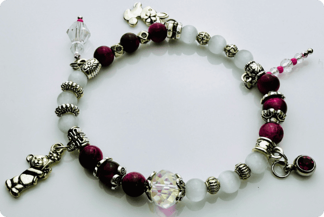 Verspieltes Damenarmband mit Anhängern wie Teddybär, Blüten und Schmuckelementen, kombiniert mit weißen und weinroten Perlen, ideal als verspieltes Accessoire.