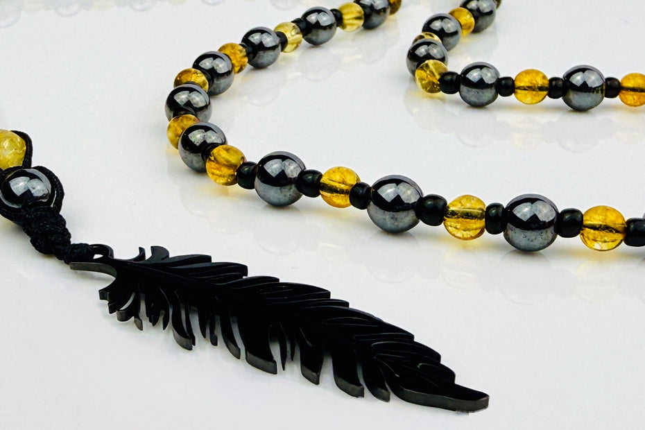 Handgefertigte Y-Halskette für Herren mit gelbem Citrin, Hämatit-Perlen und einem eleganten Edelstahl-Federnanhänger. Kunstvolle Makramee-Technik und schwarze Rocailles ergänzen das moderne und stilvolle Design.