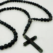 Luxuriöse schwarze Perlenkette mit glänzenden Edelstahlelementen und markantem Kreuzanhänger.
