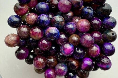 Tigerauge-Perlen in faszinierender Galaxy-Mischung aus Violett, Blau, Pink und erdigen Braunnuancen, glänzend arrangiert in einer Glasschale.
