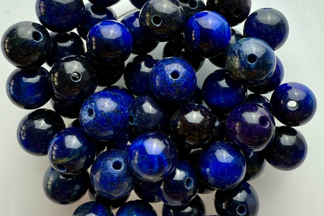 Runde Tigerauge-Perlen in tiefem Mitternachtsblau mit feinen Glanzreflexen, kunstvoll arrangiert in einer Schale.