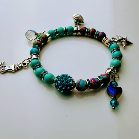 Armband im Meeresdesign mit Türkistönen, Jaspis-Perlen und Anhängern in Form von Meerjungfrau, Muschel und Fisch. Handgefertigt mit maritimen Details und funkelnden Kristallen – ideal für sommerliche Outfits.