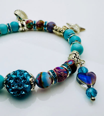 Armband im Meeresdesign mit Türkistönen, Jaspis-Perlen und Anhängern in Form von Meerjungfrau, Muschel und Fisch. Handgefertigt mit maritimen Details und funkelnden Kristallen – ideal für sommerliche Outfits.