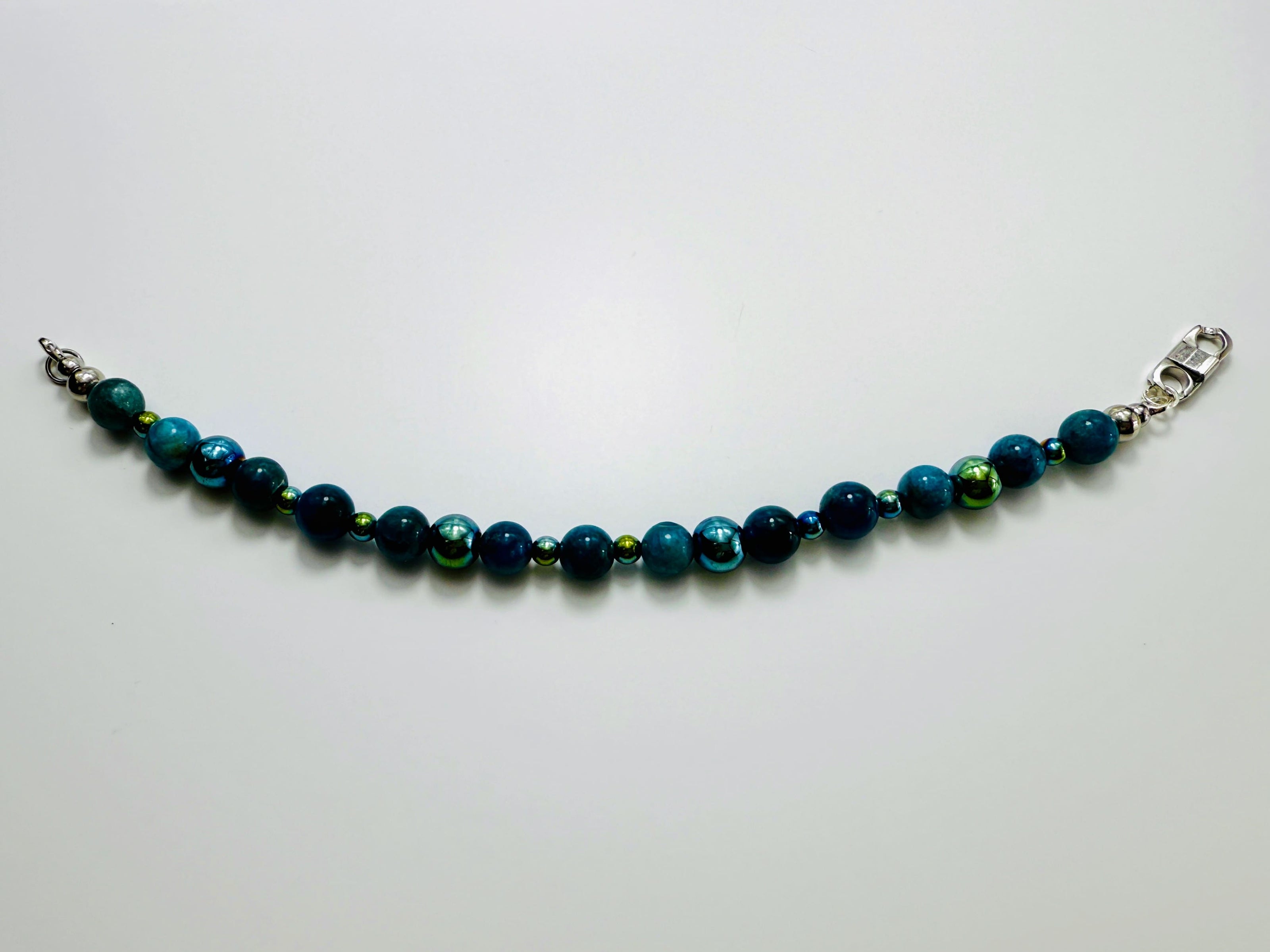 Armband aus blauen Apatit-Perlen und facettiertem Hämatit auf weißem Hintergrund, aufgefächert dargestellt.