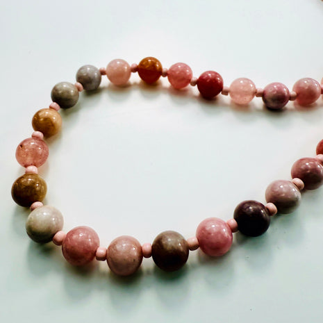 Detailansicht der Farbverläufe der runden Erdbeerquarz-Perlen in Rosa- und Brauntönen.