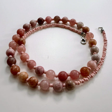 Halskette aus rosa Erdbeerquarz-Perlen und Rocailles mit Edelstahlverschluss, flach fotografiert.