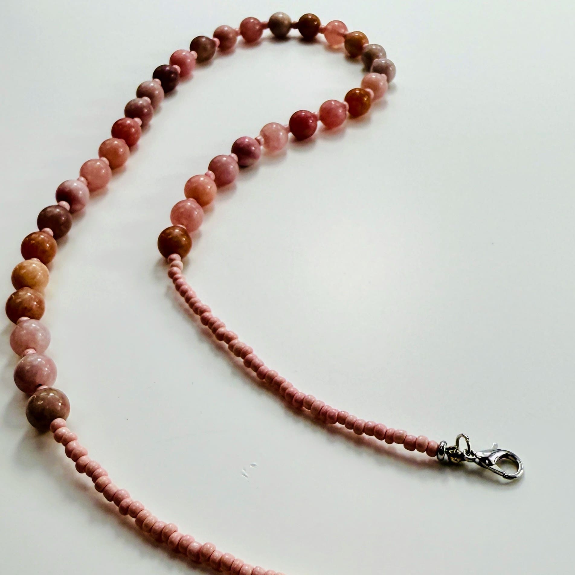 Halskette aus rosa Erdbeerquarz-Perlen und Rocailles mit Edelstahlverschluss, flach fotografiert.