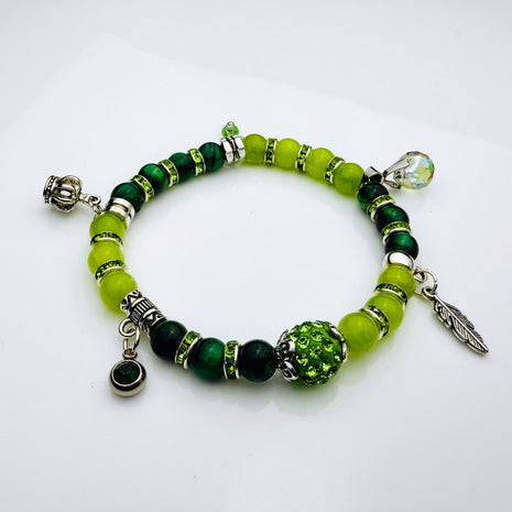 Frühlingshaftes Damenarmband mit strahlend grünen Perlen, glitzernden Strass-Elementen und filigranem Feder-Anhänger. Handgefertigt in der Schweiz, ideal für leichte Frühlingsoutfits.