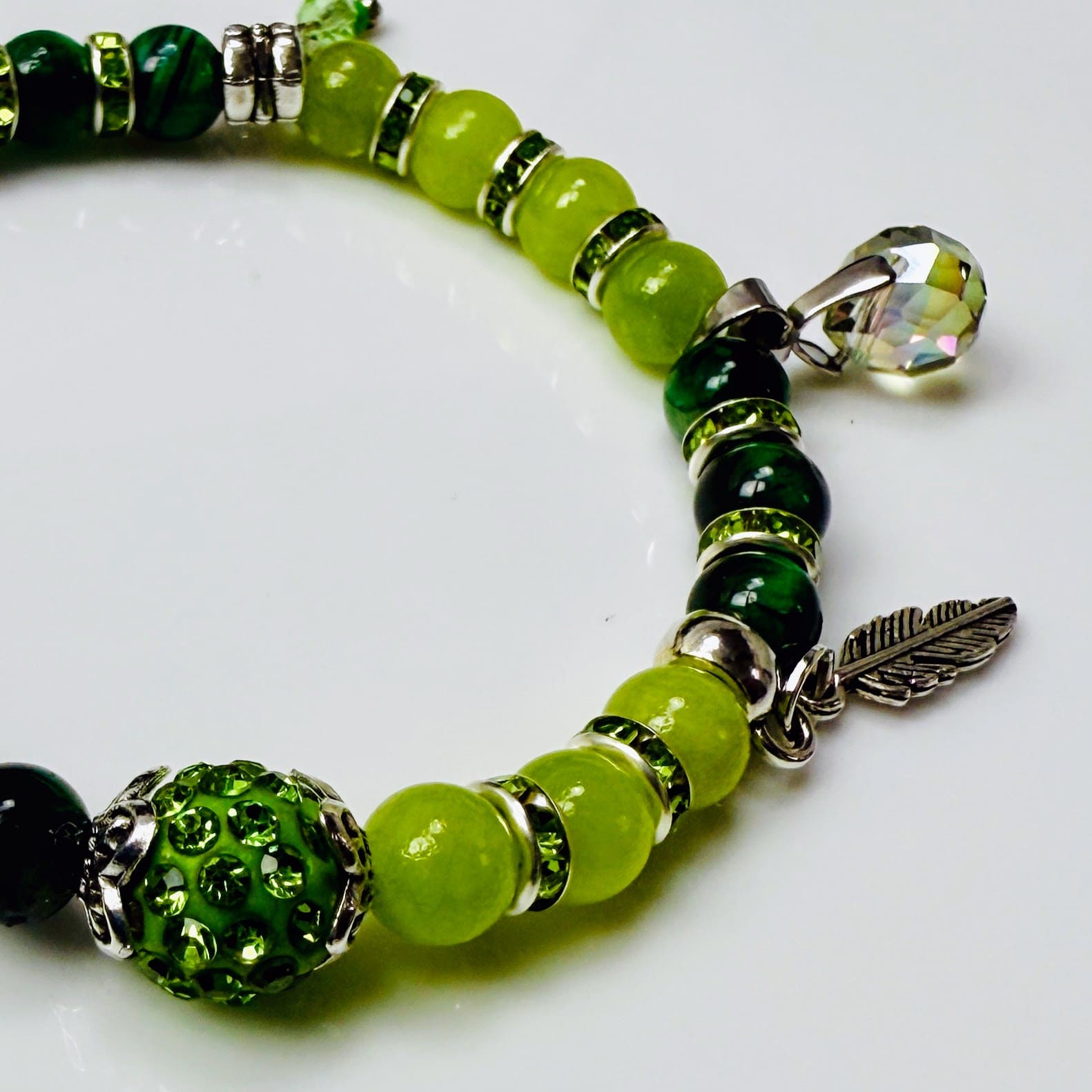 Frühlingshaftes Damenarmband mit strahlend grünen Perlen, glitzernden Strass-Elementen und filigranem Feder-Anhänger. Handgefertigt in der Schweiz, ideal für leichte Frühlingsoutfits.