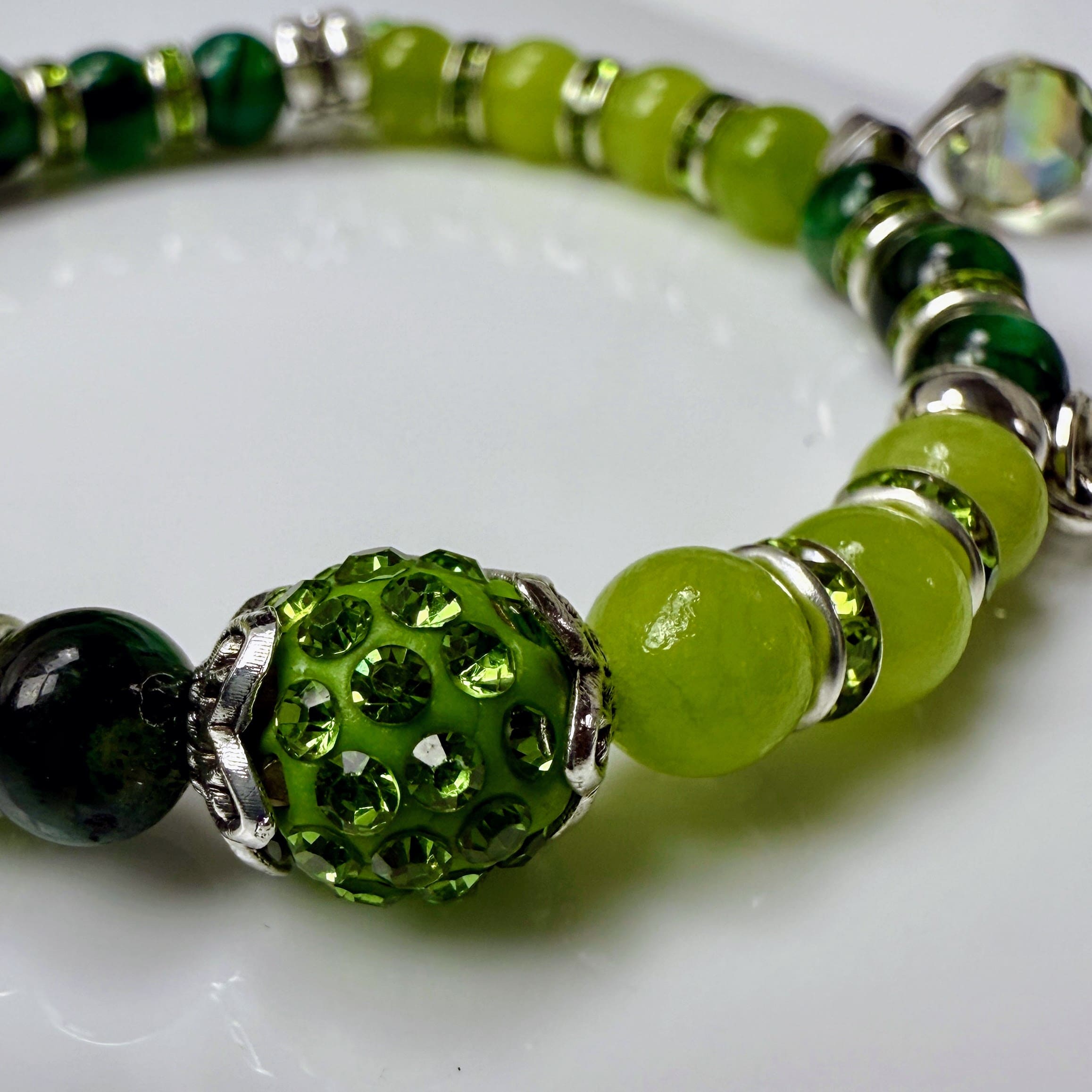 Frühlingshaftes Damenarmband mit strahlend grünen Perlen, glitzernden Strass-Elementen und filigranem Feder-Anhänger. Handgefertigt in der Schweiz, ideal für leichte Frühlingsoutfits.