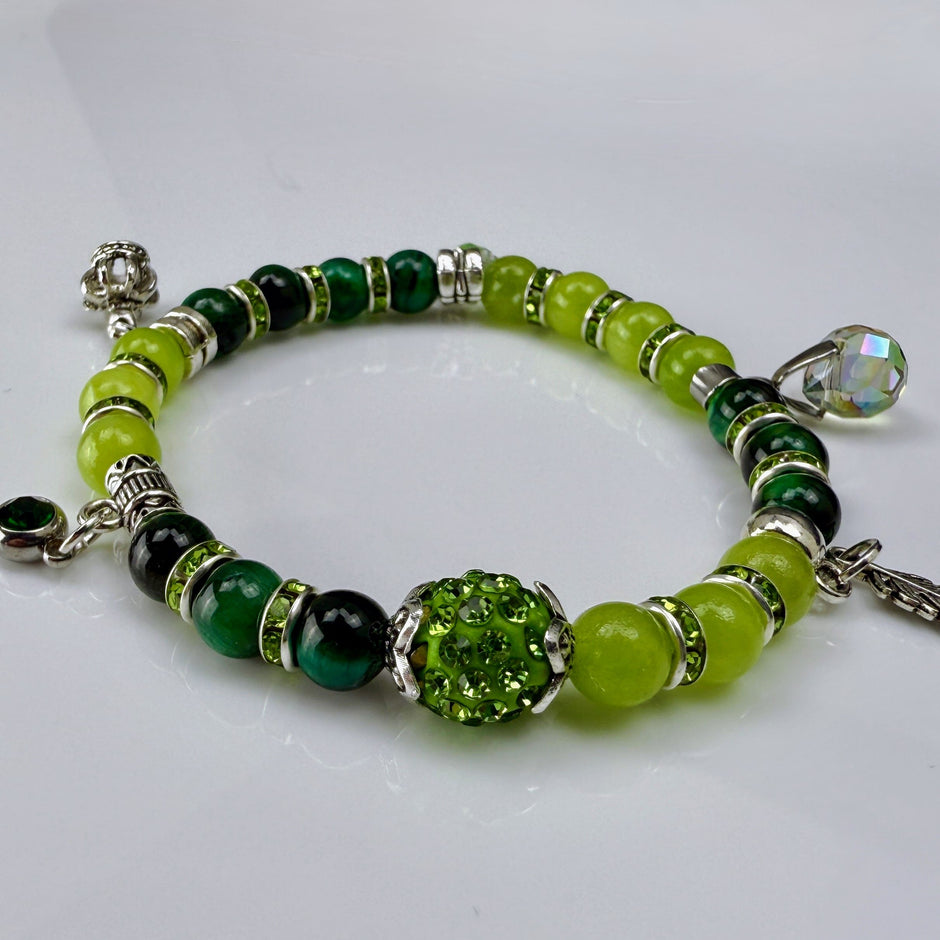 Frühlingshaftes Damenarmband mit strahlend grünen Perlen, glitzernden Strass-Elementen und filigranem Feder-Anhänger. Handgefertigt in der Schweiz, ideal für leichte Frühlingsoutfits.