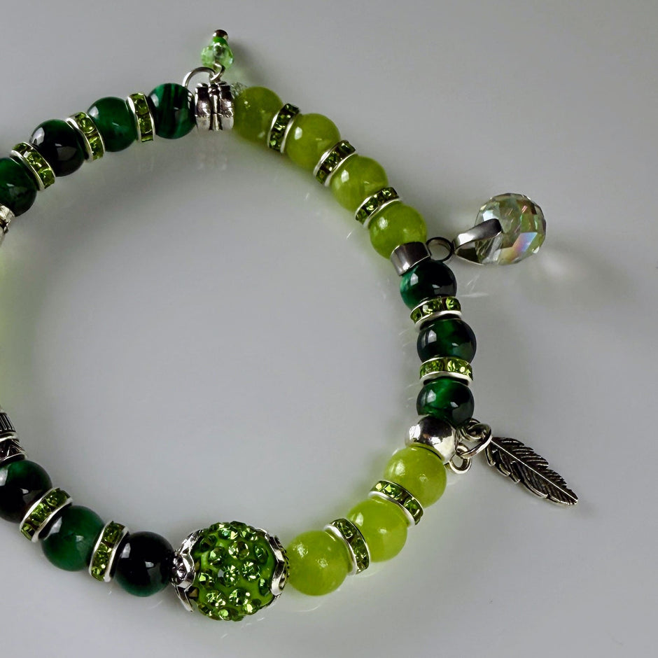 Frühlingshaftes Damenarmband mit strahlend grünen Perlen, glitzernden Strass-Elementen und filigranem Feder-Anhänger. Handgefertigt in der Schweiz, ideal für leichte Frühlingsoutfits.