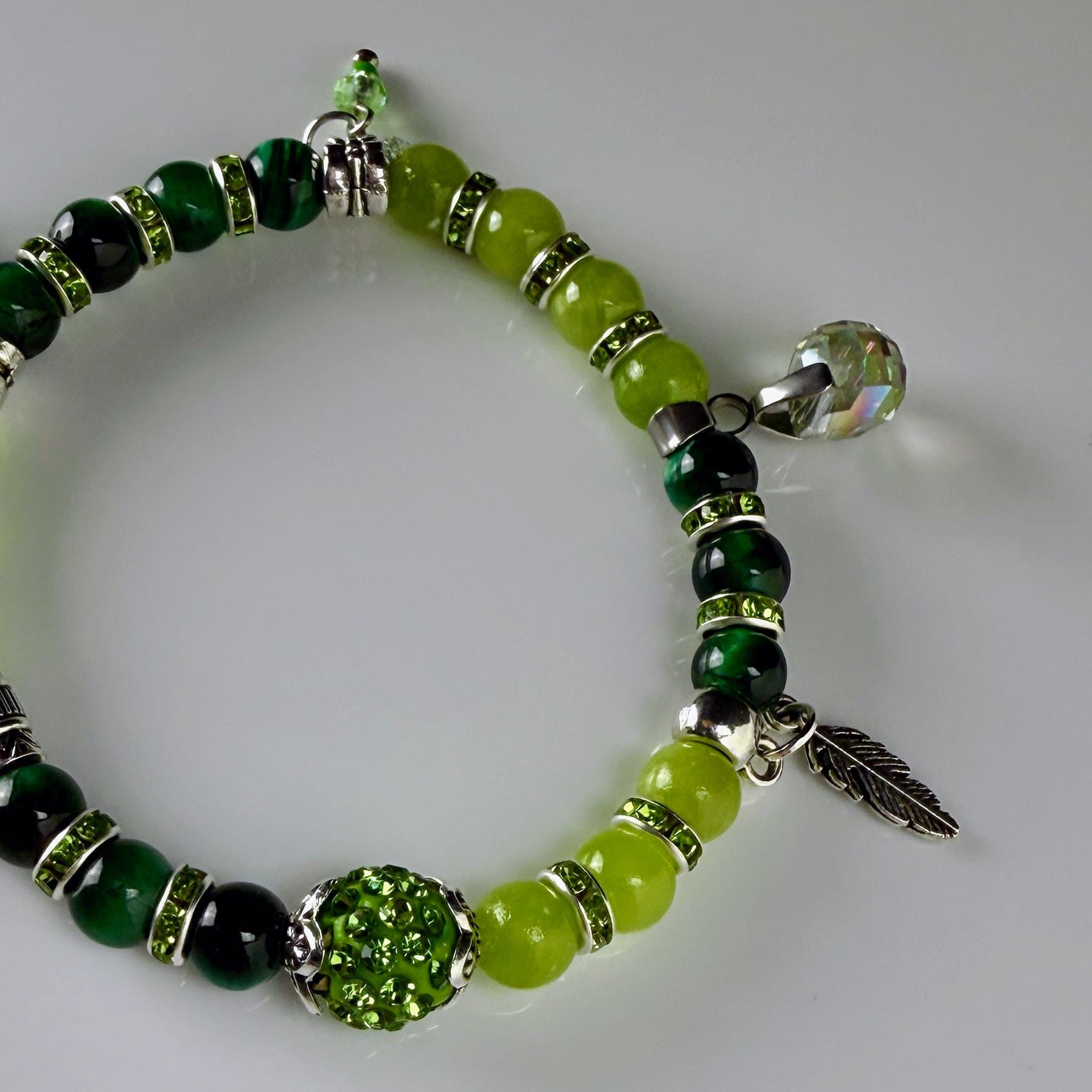 Frühlingshaftes Damenarmband mit strahlend grünen Perlen, glitzernden Strass-Elementen und filigranem Feder-Anhänger. Handgefertigt in der Schweiz, ideal für leichte Frühlingsoutfits.