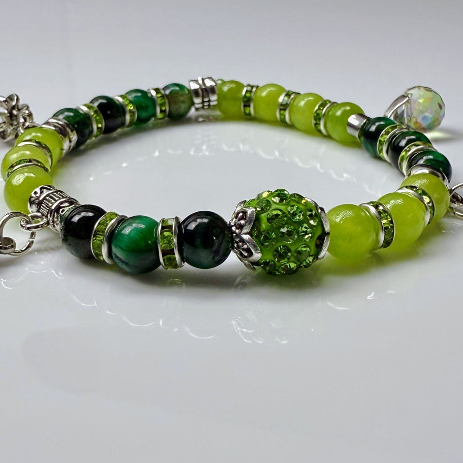 Frühlingshaftes Damenarmband mit strahlend grünen Perlen, glitzernden Strass-Elementen und filigranem Feder-Anhänger. Handgefertigt in der Schweiz, ideal für leichte Frühlingsoutfits.