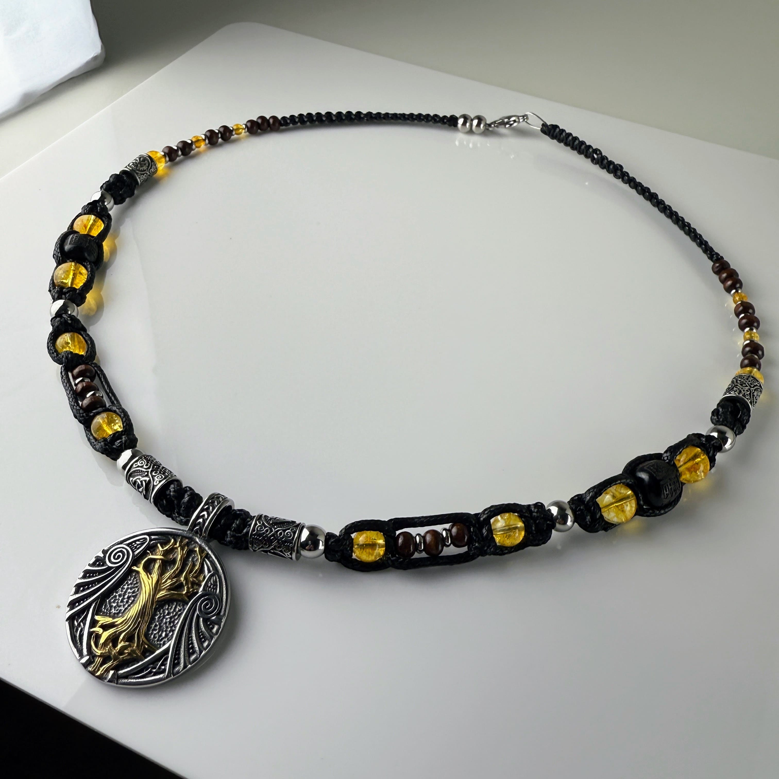 Handgeknüpfte Makramee-Kette mit funkelnden Citrin-Steinperlen, edlen Edelstahlelementen und einem kunstvoll verzierten Runenanhänger. Schweizer Schmuckstück, das Eleganz und Mystik verbindet.