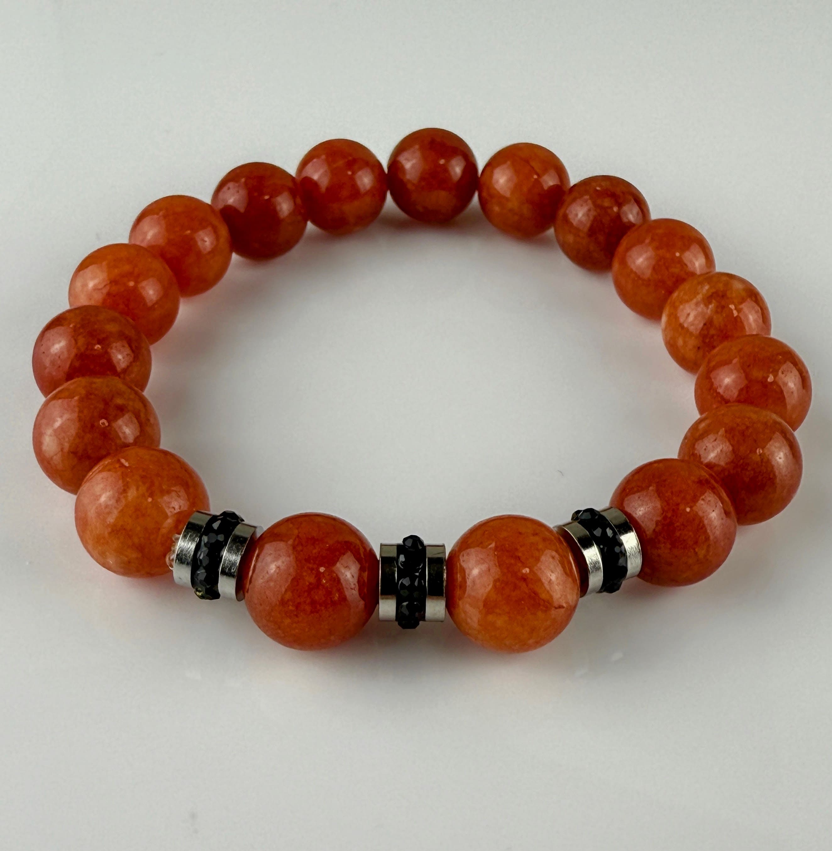 Handgefertigtes Armband mit leuchtenden Karneol-Quarz-Perlen in Orange-Rot, verziert mit eleganten Edelstahl-Elementen und funkelnden schwarzen Kristallakzenten. Ein modernes Accessoire mit lebendigen Farben und hochwertiger Verarbeitung.