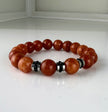 Handgefertigtes Armband mit leuchtenden Karneol-Quarz-Perlen in Orange-Rot, verziert mit eleganten Edelstahl-Elementen und funkelnden schwarzen Kristallakzenten. Ein modernes Accessoire mit lebendigen Farben und hochwertiger Verarbeitung.