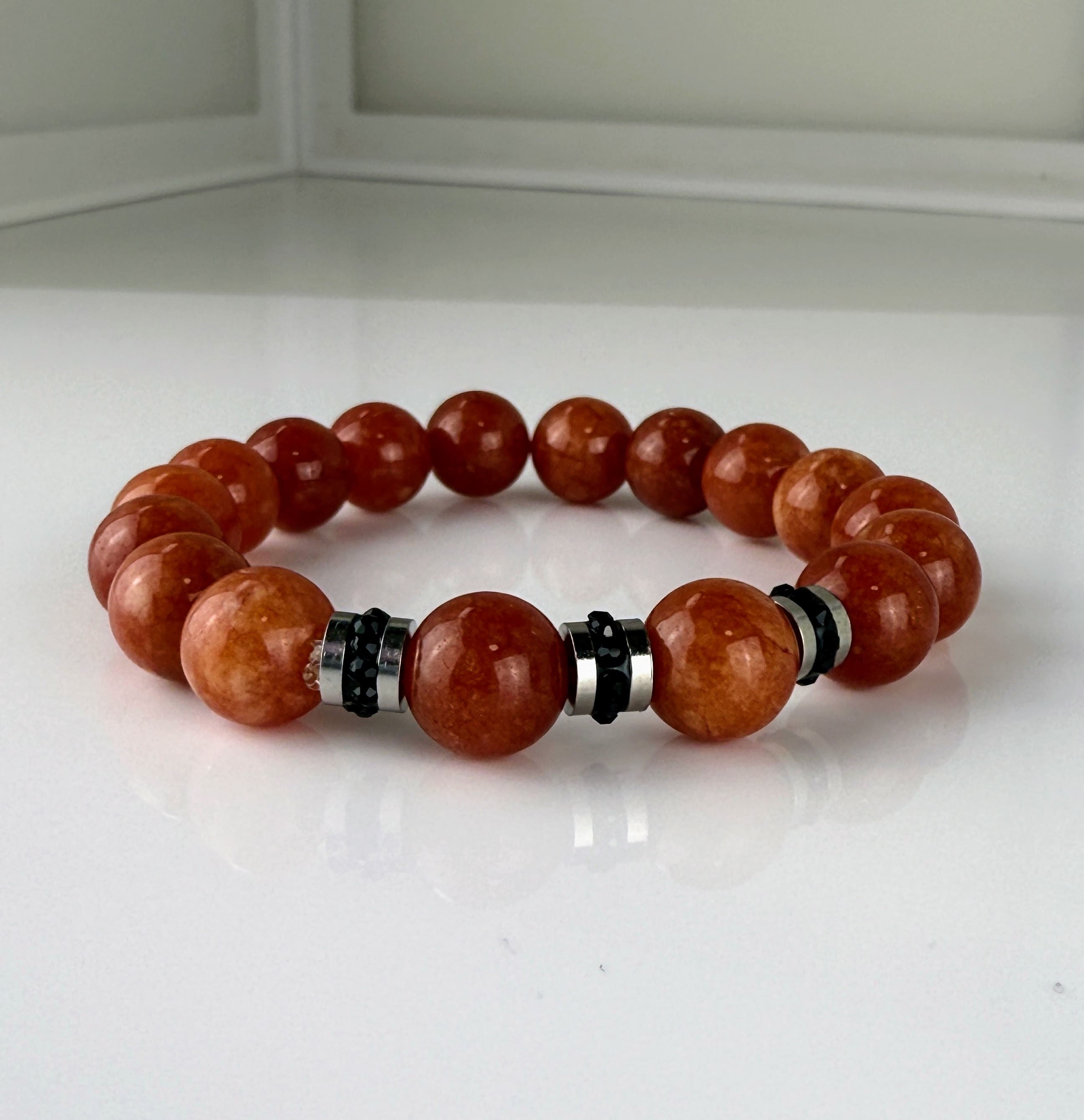 Handgefertigtes Armband mit leuchtenden Karneol-Quarz-Perlen in Orange-Rot, verziert mit eleganten Edelstahl-Elementen und funkelnden schwarzen Kristallakzenten. Ein modernes Accessoire mit lebendigen Farben und hochwertiger Verarbeitung.