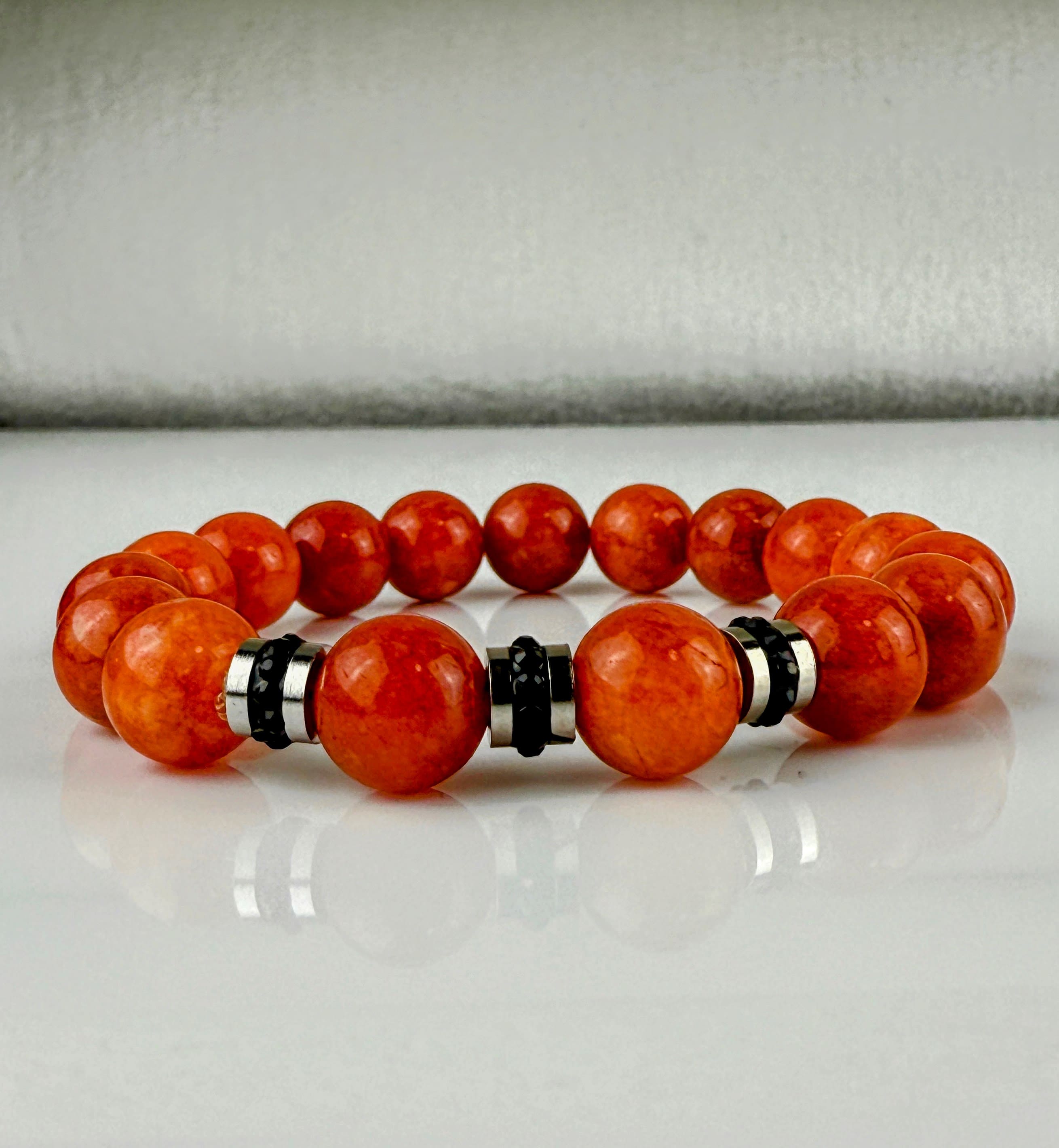 Handgefertigtes Armband mit leuchtenden Karneol-Quarz-Perlen in Orange-Rot, verziert mit eleganten Edelstahl-Elementen und funkelnden schwarzen Kristallakzenten. Ein modernes Accessoire mit lebendigen Farben und hochwertiger Verarbeitung.