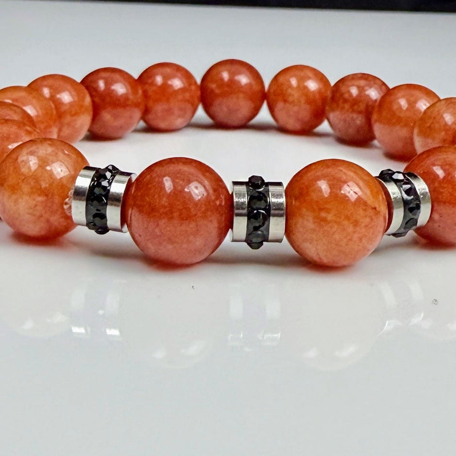 Handgefertigtes Armband mit leuchtenden Karneol-Quarz-Perlen in Orange-Rot, verziert mit eleganten Edelstahl-Elementen und funkelnden schwarzen Kristallakzenten. Ein modernes Accessoire mit lebendigen Farben und hochwertiger Verarbeitung.