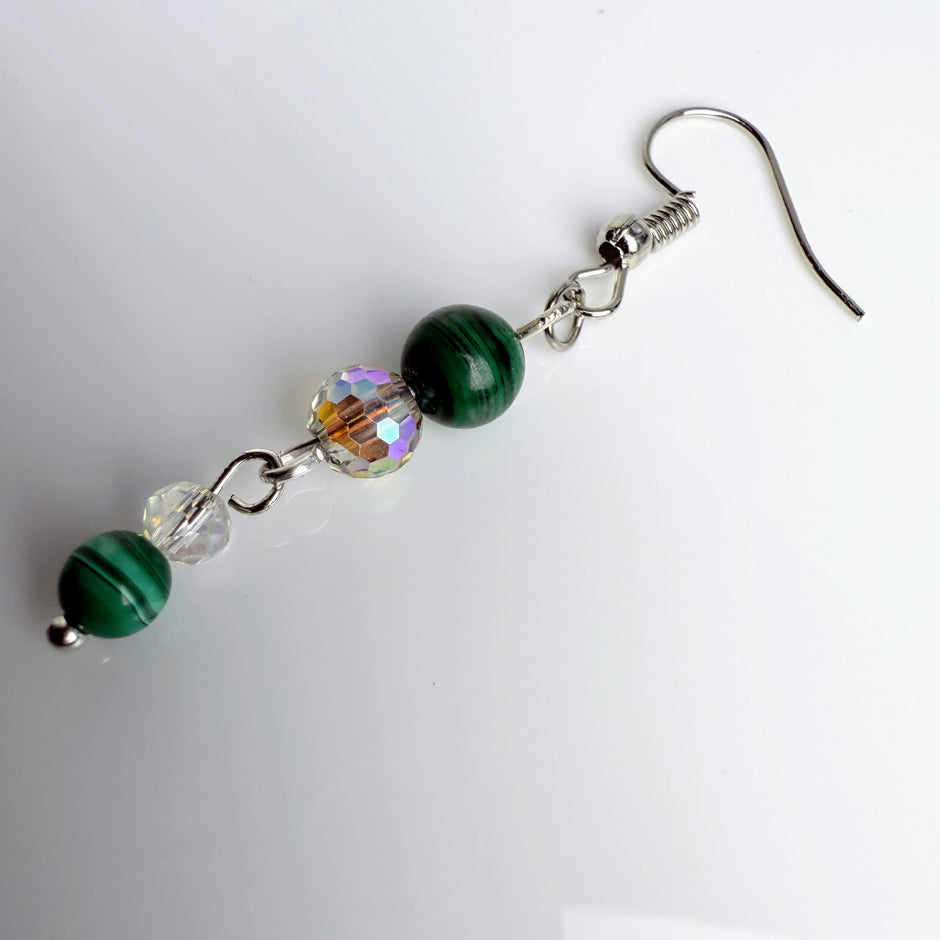 Zierliche Ohrhänger mit grünen Malachitperlen, facettierten Glasperlen und Edelstahlhaken, stilvoll fotografiert.