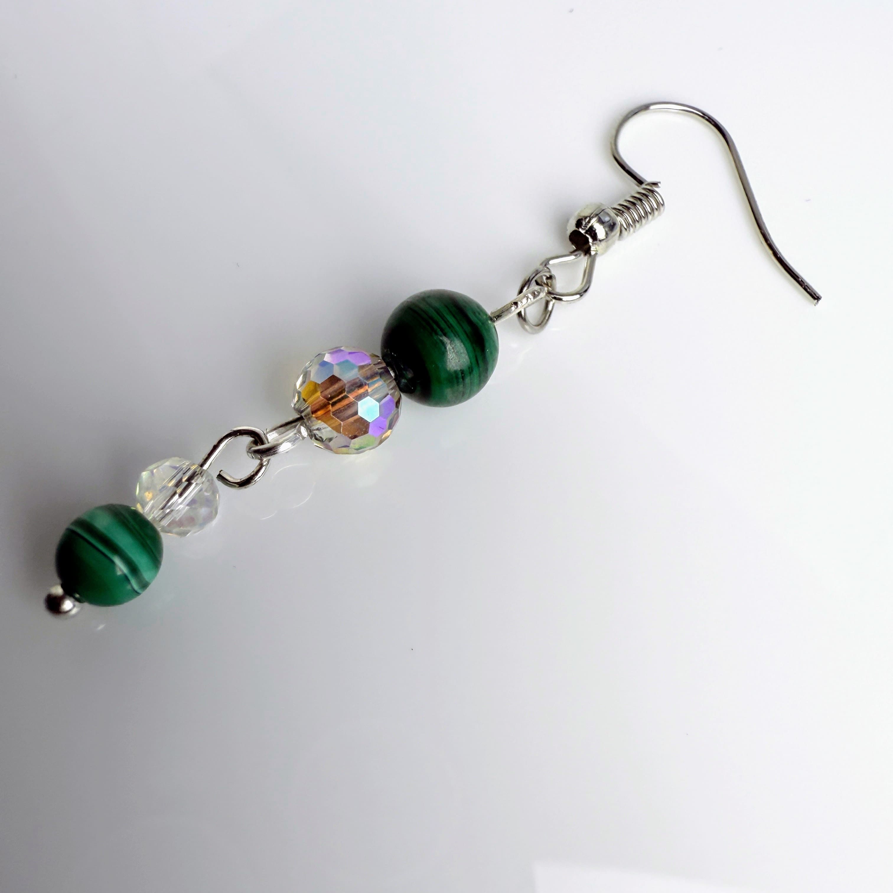 Zierliche Ohrhänger mit grünen Malachitperlen, facettierten Glasperlen und Edelstahlhaken, stilvoll fotografiert.
