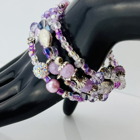 Handgefertigtes Spiralarmband in zarten Rosa- und Fliedertönen mit funkelnden Glasperlen, Strass-Elementen und filigranen Metall-Details. Flexibel und elegant, perfekt für besondere Anlässe und den Alltag.