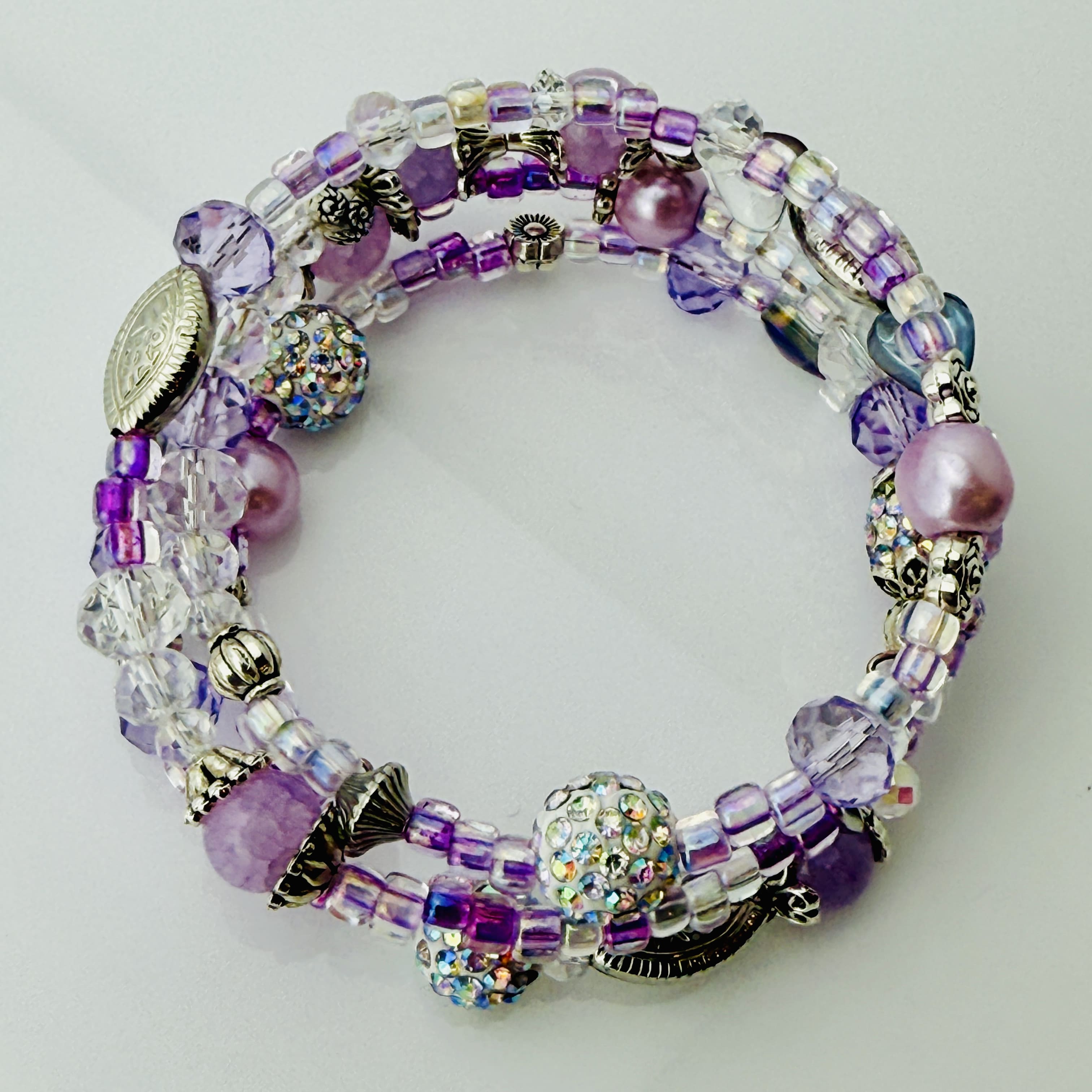 Handgefertigtes Spiralarmband in zarten Rosa- und Fliedertönen mit funkelnden Glasperlen, Strass-Elementen und filigranen Metall-Details. Flexibel und elegant, perfekt für besondere Anlässe und den Alltag.