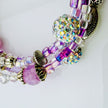 Handgefertigtes Spiralarmband in zarten Rosa- und Fliedertönen mit funkelnden Glasperlen, Strass-Elementen und filigranen Metall-Details. Flexibel und elegant, perfekt für besondere Anlässe und den Alltag.