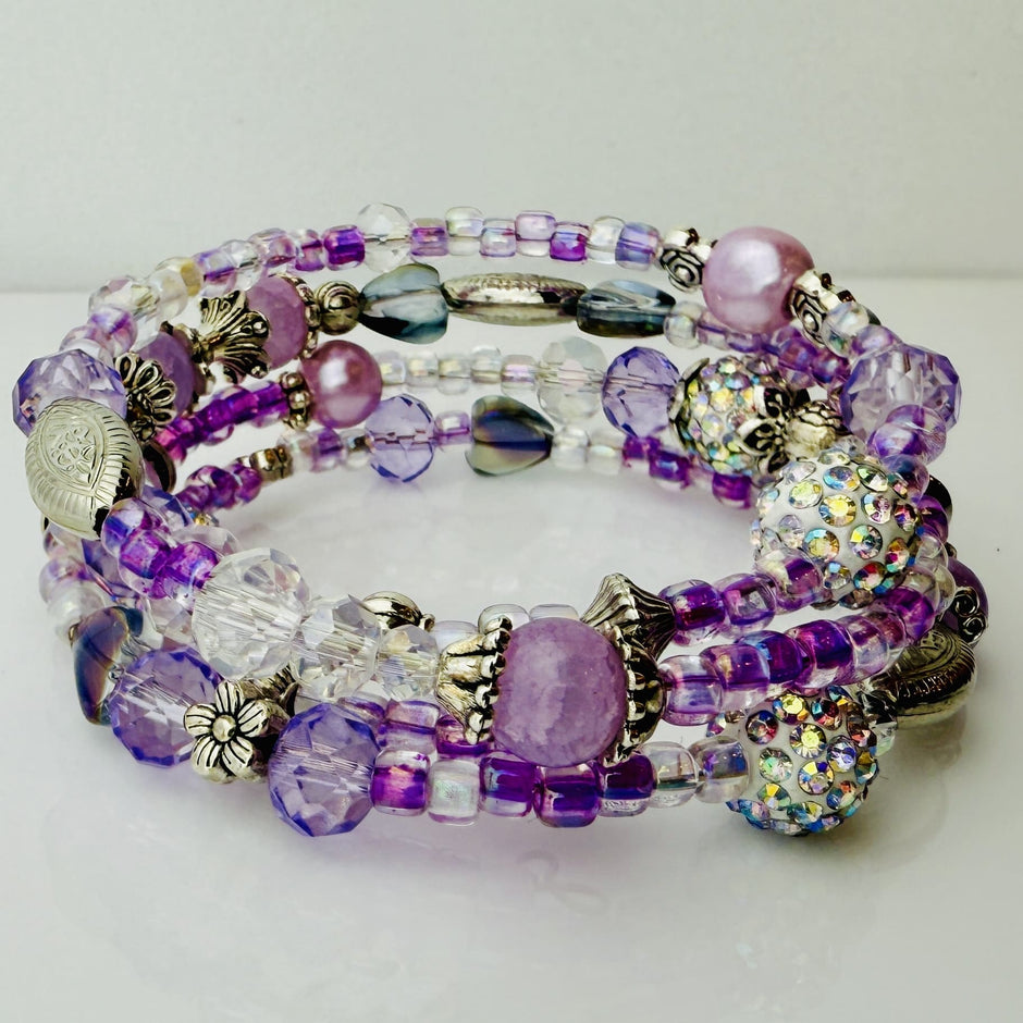 Handgefertigtes Spiralarmband in zarten Rosa- und Fliedertönen mit funkelnden Glasperlen, Strass-Elementen und filigranen Metall-Details. Flexibel und elegant, perfekt für besondere Anlässe und den Alltag.