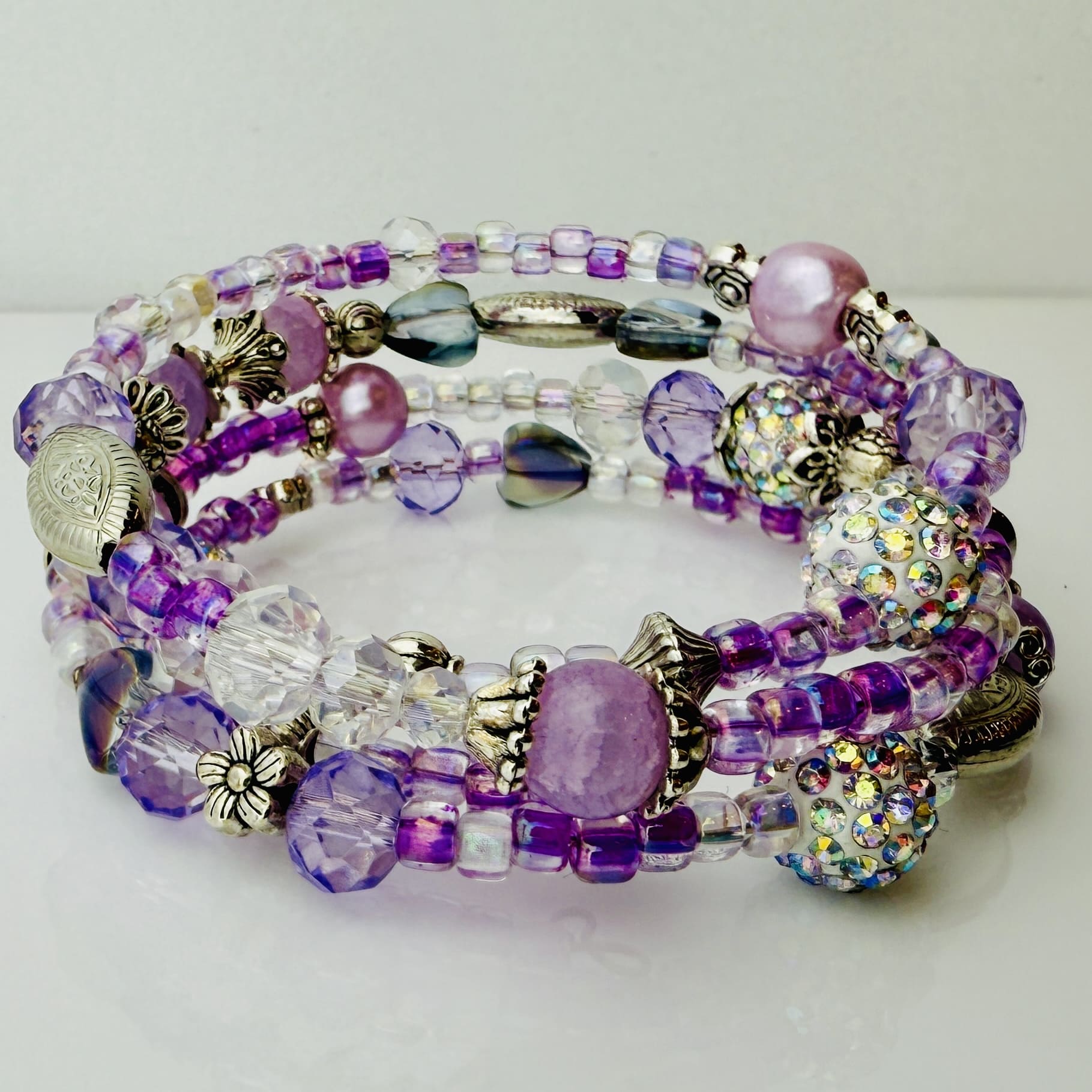 Handgefertigtes Spiralarmband in zarten Rosa- und Fliedertönen mit funkelnden Glasperlen, Strass-Elementen und filigranen Metall-Details. Flexibel und elegant, perfekt für besondere Anlässe und den Alltag.