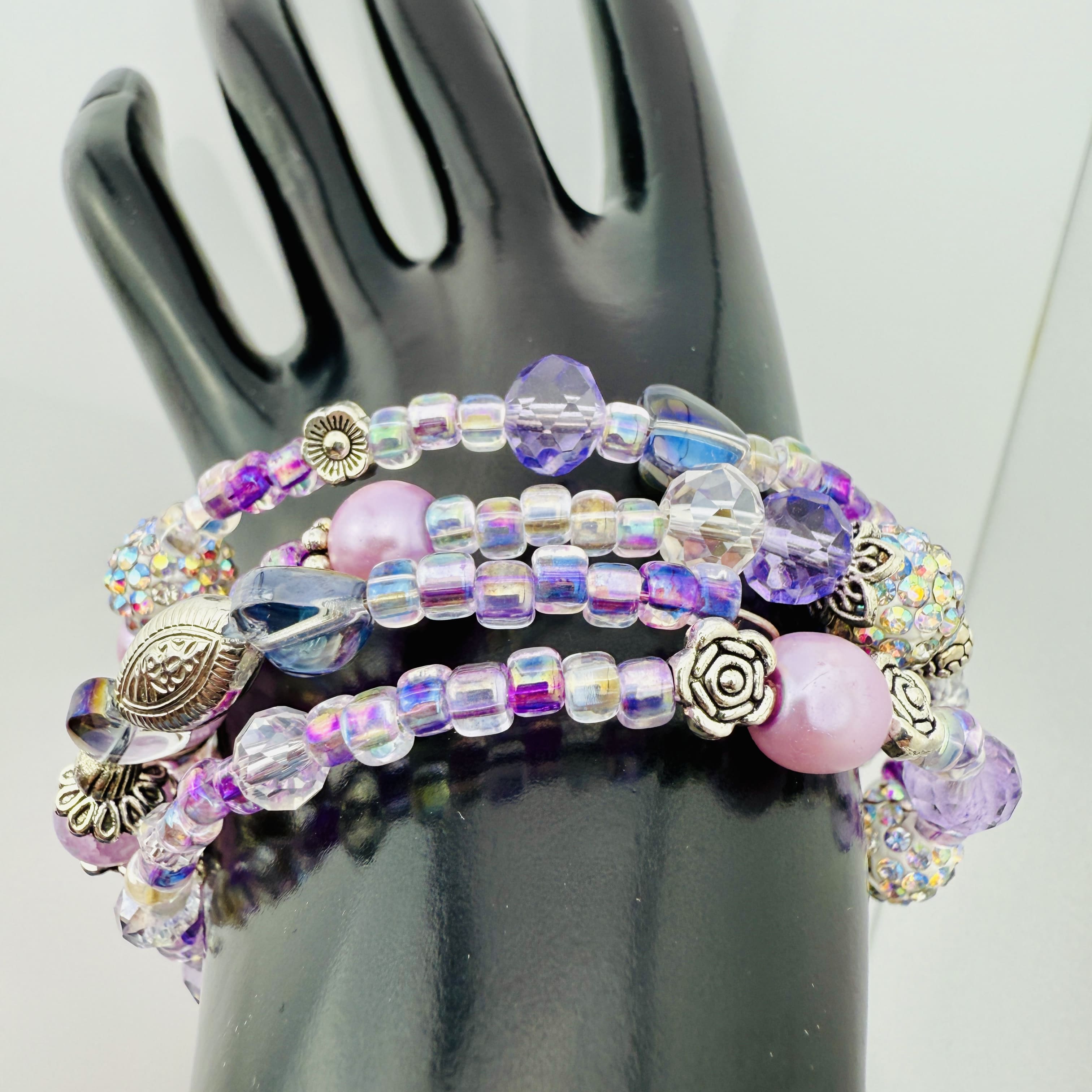 Handgefertigtes Spiralarmband in zarten Rosa- und Fliedertönen mit funkelnden Glasperlen, Strass-Elementen und filigranen Metall-Details. Flexibel und elegant, perfekt für besondere Anlässe und den Alltag.
