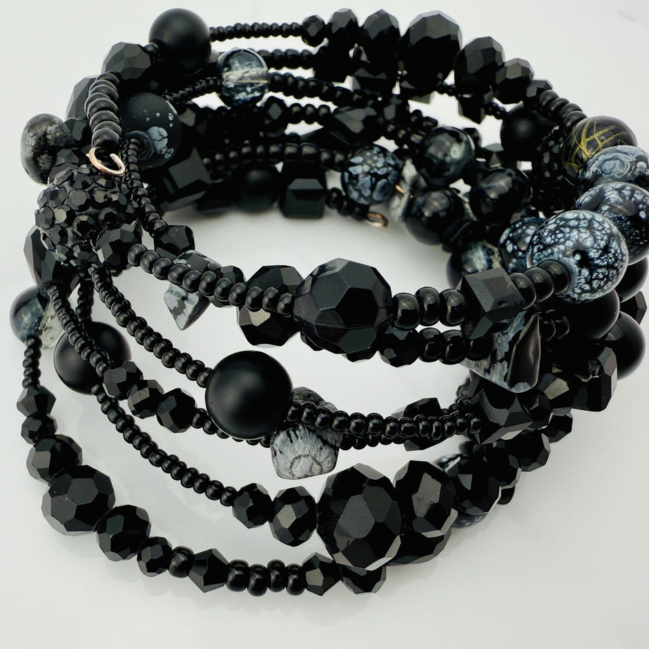 Elegantes spiralförmiges Armband mit einer vielseitigen Kombination aus schwarzen Glasperlen in verschiedenen Größen und Oberflächen. Handgefertigt in der Schweiz, flexibel ohne Verschluss, perfekt für stilvolle Alltagslooks und besondere Anlässe.