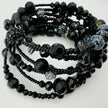 Elegantes spiralförmiges Armband mit einer vielseitigen Kombination aus schwarzen Glasperlen in verschiedenen Größen und Oberflächen. Handgefertigt in der Schweiz, flexibel ohne Verschluss, perfekt für stilvolle Alltagslooks und besondere Anlässe.