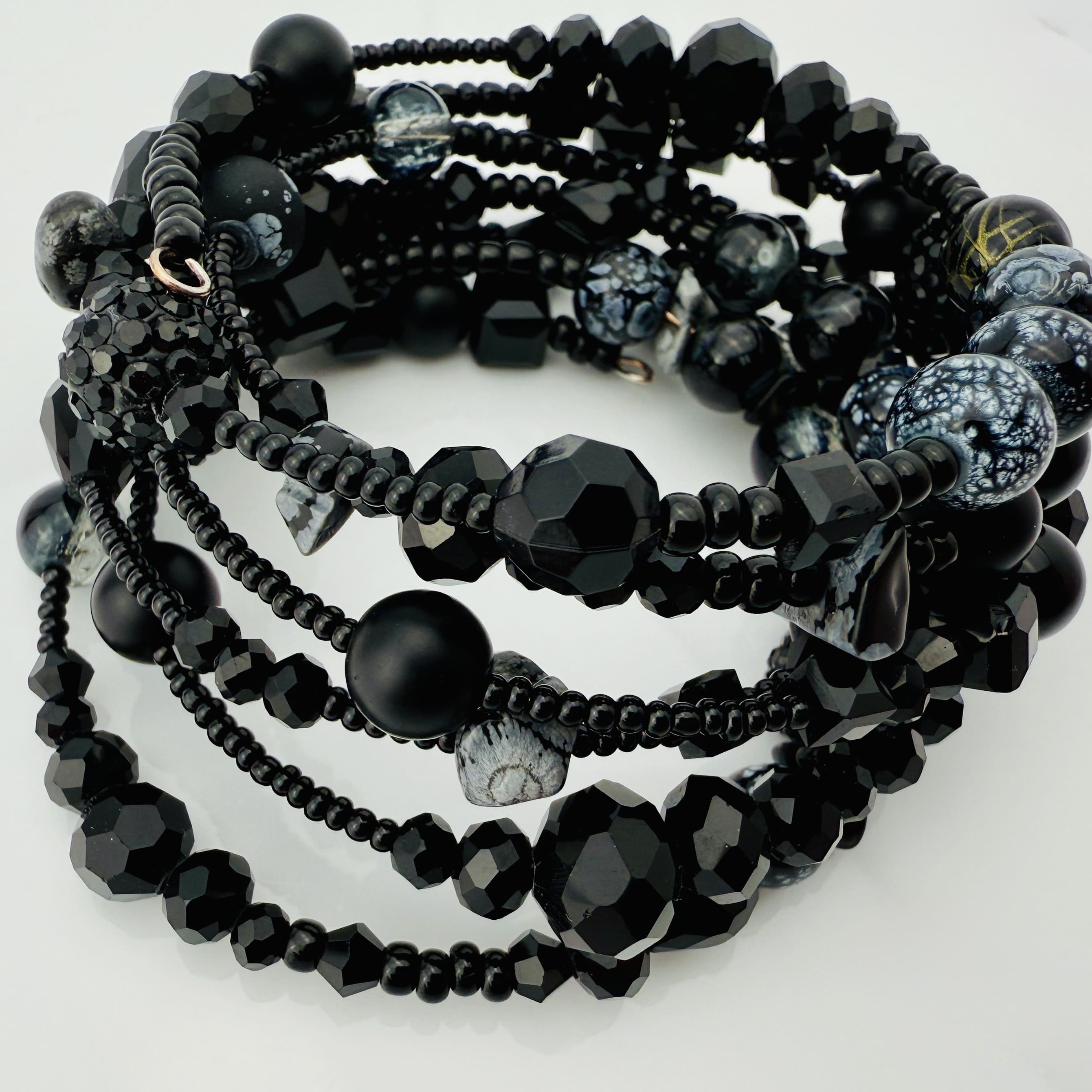 Elegantes spiralförmiges Armband mit einer vielseitigen Kombination aus schwarzen Glasperlen in verschiedenen Größen und Oberflächen. Handgefertigt in der Schweiz, flexibel ohne Verschluss, perfekt für stilvolle Alltagslooks und besondere Anlässe.