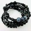 Elegantes spiralförmiges Armband mit einer vielseitigen Kombination aus schwarzen Glasperlen in verschiedenen Größen und Oberflächen. Handgefertigt in der Schweiz, flexibel ohne Verschluss, perfekt für stilvolle Alltagslooks und besondere Anlässe.