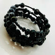 Elegantes spiralförmiges Armband mit einer vielseitigen Kombination aus schwarzen Glasperlen in verschiedenen Größen und Oberflächen. Handgefertigt in der Schweiz, flexibel ohne Verschluss, perfekt für stilvolle Alltagslooks und besondere Anlässe.