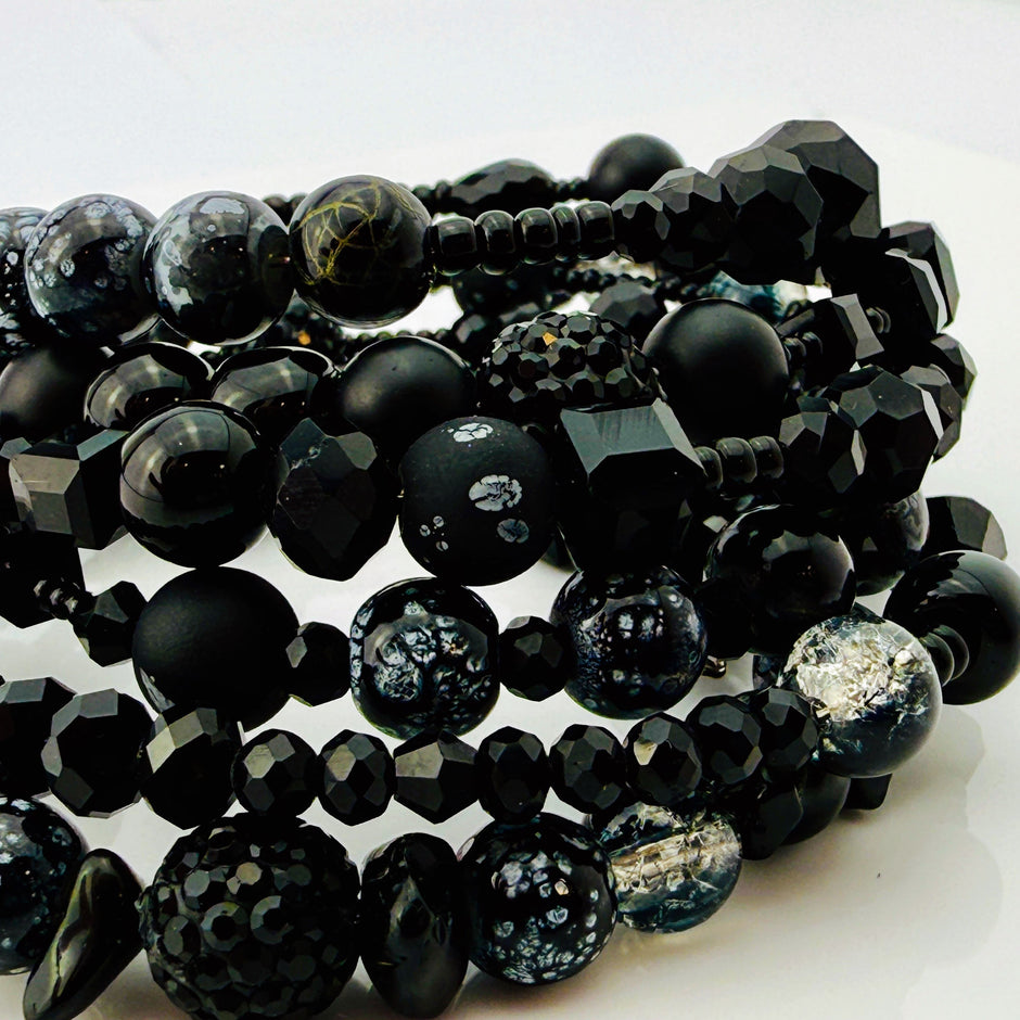 Elegantes spiralförmiges Armband mit einer vielseitigen Kombination aus schwarzen Glasperlen in verschiedenen Größen und Oberflächen. Handgefertigt in der Schweiz, flexibel ohne Verschluss, perfekt für stilvolle Alltagslooks und besondere Anlässe.