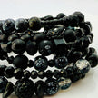 Elegantes spiralförmiges Armband mit einer vielseitigen Kombination aus schwarzen Glasperlen in verschiedenen Größen und Oberflächen. Handgefertigt in der Schweiz, flexibel ohne Verschluss, perfekt für stilvolle Alltagslooks und besondere Anlässe.