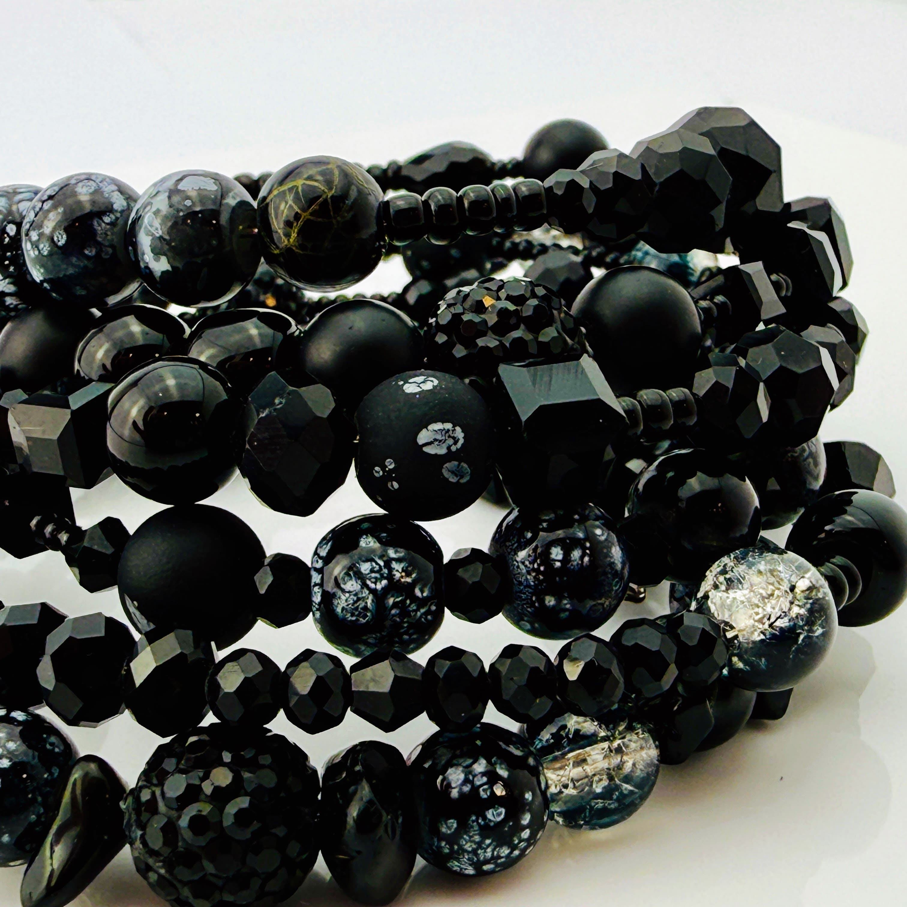 Elegantes spiralförmiges Armband mit einer vielseitigen Kombination aus schwarzen Glasperlen in verschiedenen Größen und Oberflächen. Handgefertigt in der Schweiz, flexibel ohne Verschluss, perfekt für stilvolle Alltagslooks und besondere Anlässe.