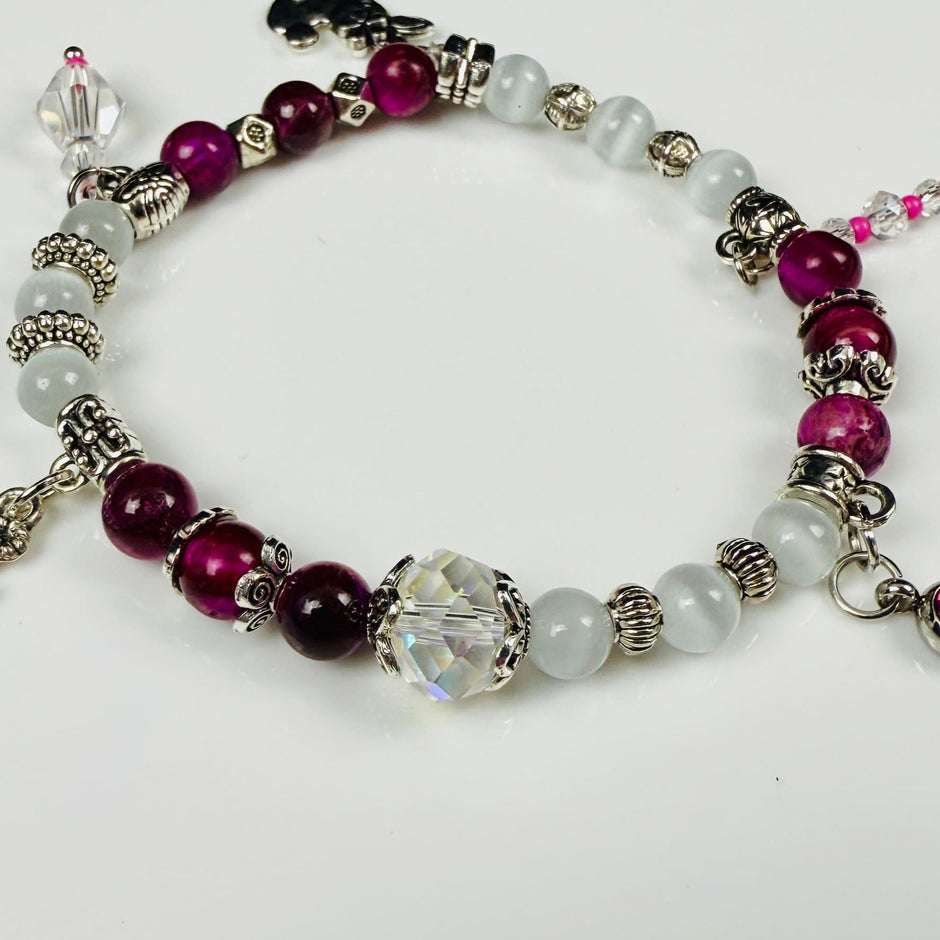 Verspieltes Damenarmband mit Anhängern wie Teddybär, Blüten und Schmuckelementen, kombiniert mit weißen und weinroten Perlen, ideal als verspieltes Accessoire.