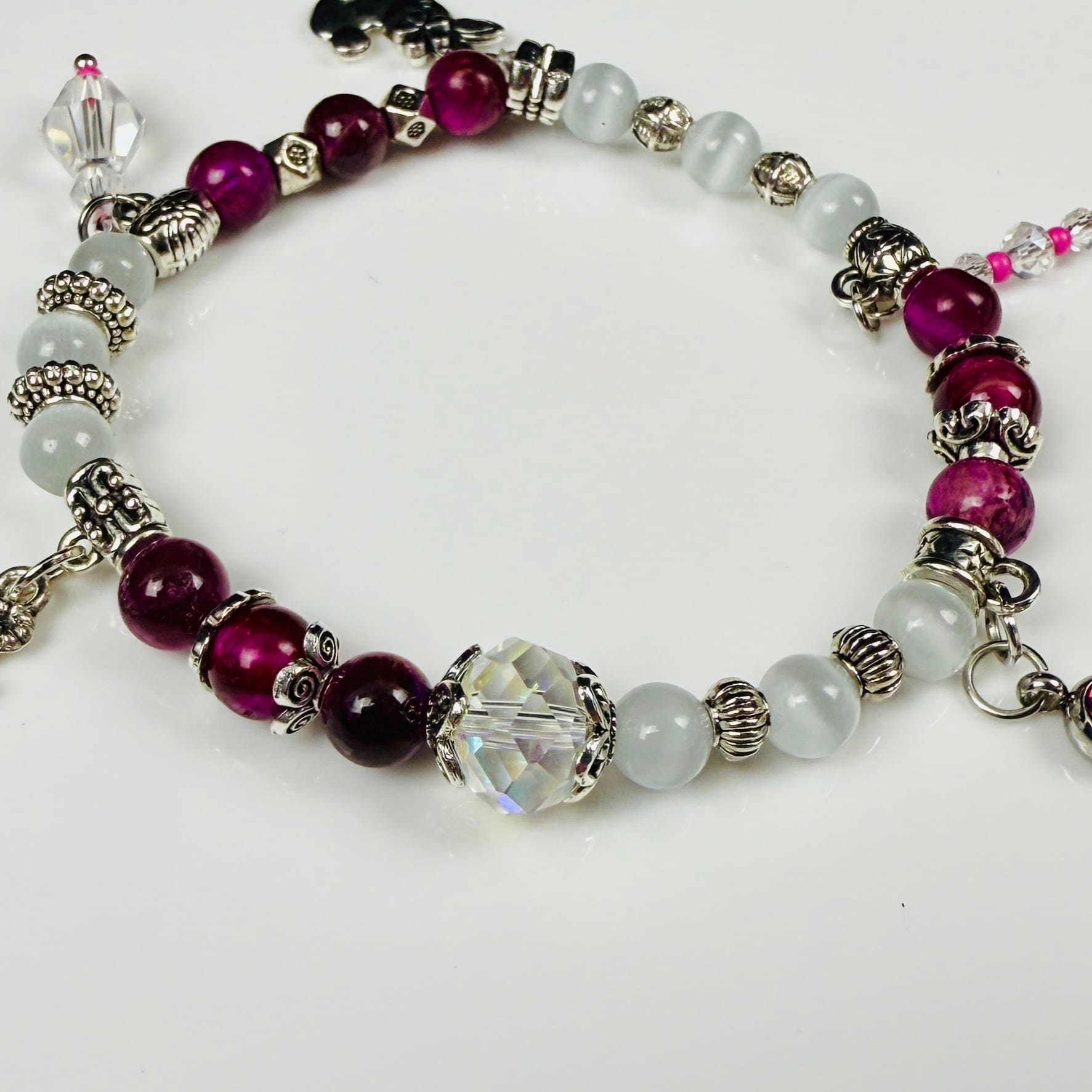 Verspieltes Damenarmband mit Anhängern wie Teddybär, Blüten und Schmuckelementen, kombiniert mit weißen und weinroten Perlen, ideal als verspieltes Accessoire.