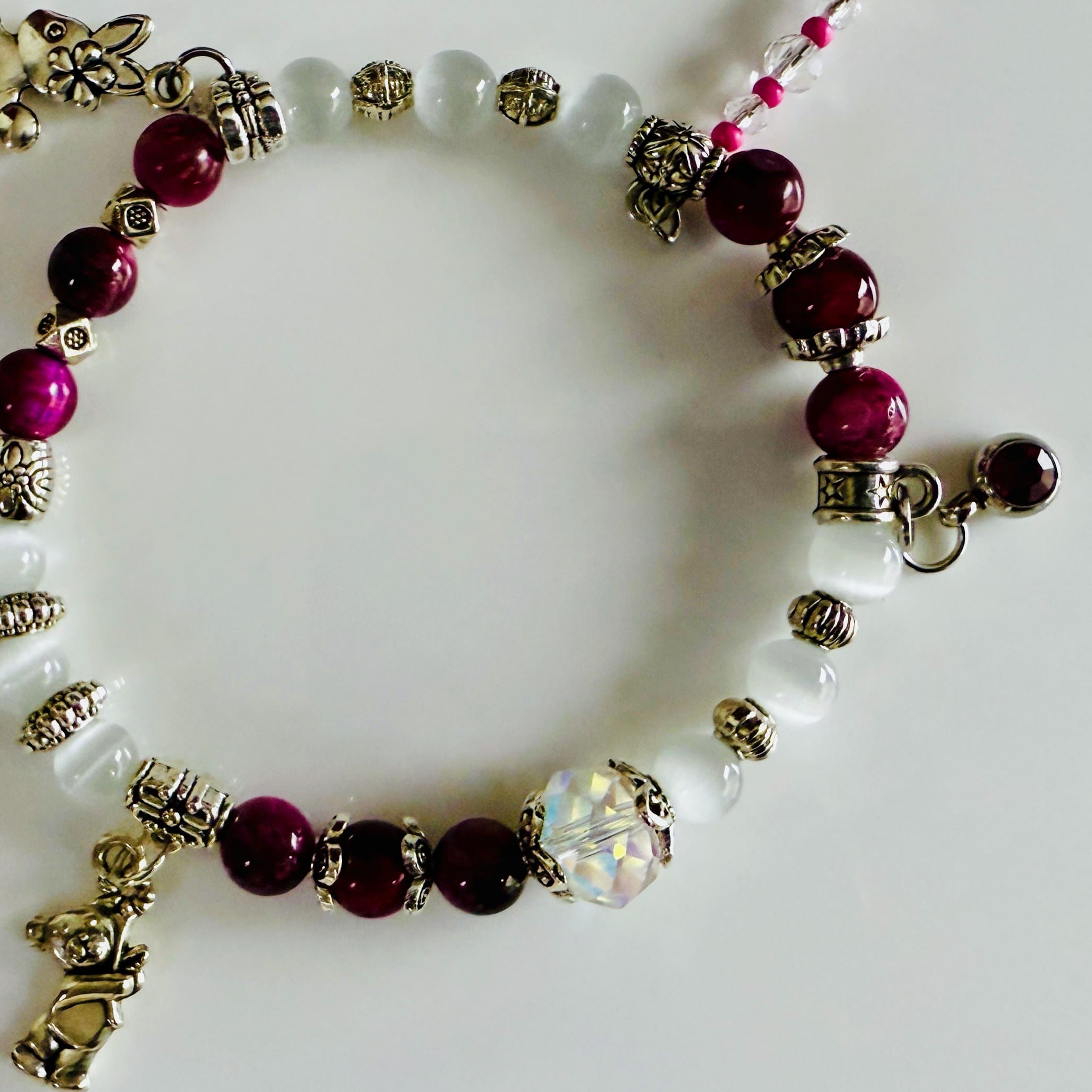 Verspieltes Damenarmband mit Anhängern wie Teddybär, Blüten und Schmuckelementen, kombiniert mit weißen und weinroten Perlen, ideal als verspieltes Accessoire.