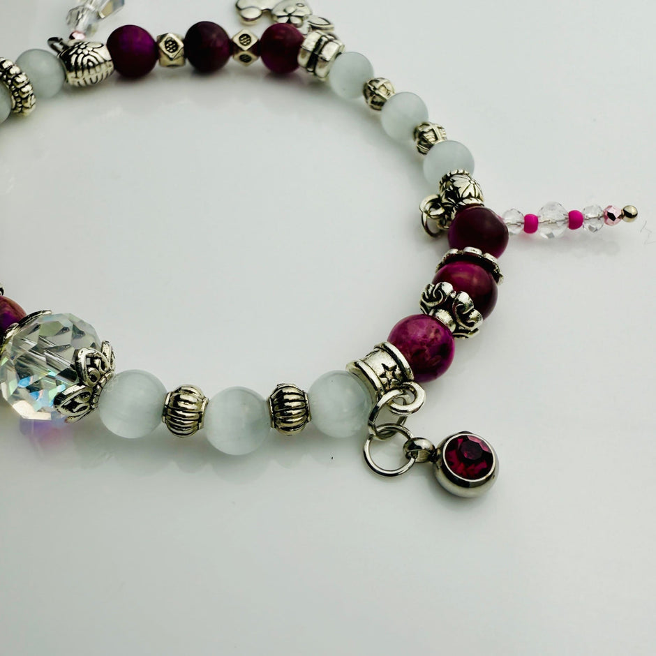 Verspieltes Damenarmband mit Anhängern wie Teddybär, Blüten und Schmuckelementen, kombiniert mit weißen und weinroten Perlen, ideal als verspieltes Accessoire.
