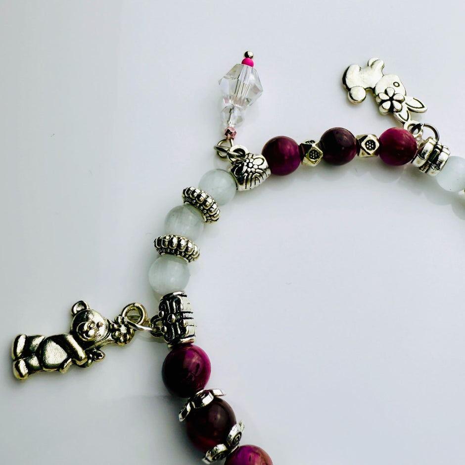 Verspieltes Damenarmband mit Anhängern wie Teddybär, Blüten und Schmuckelementen, kombiniert mit weißen und weinroten Perlen, ideal als verspieltes Accessoire.
